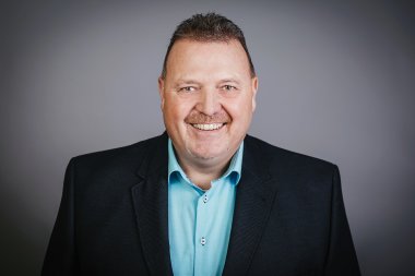 Ein Herr mit dunkelblondem Haar, türkisfarbenem Hemd und schwarzem Sacko