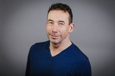 Ein Herr mit dunklen Haaren und einem blauen Pullover