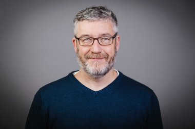 Ein Herr mit grauem Haar, grauem Bart, Brille und blauem Pullover