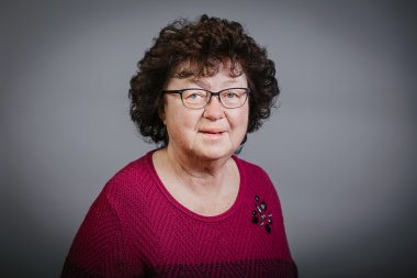 Eine Frau mit dunklen kurzen Locken, einer Brille und Fuchsia farbenem Pullover
