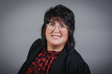 Eine schwarzhaarige Frau mit Brille, einer rot schwarzer Bluse im Leopardenmuster und einem schwarzen Jacket